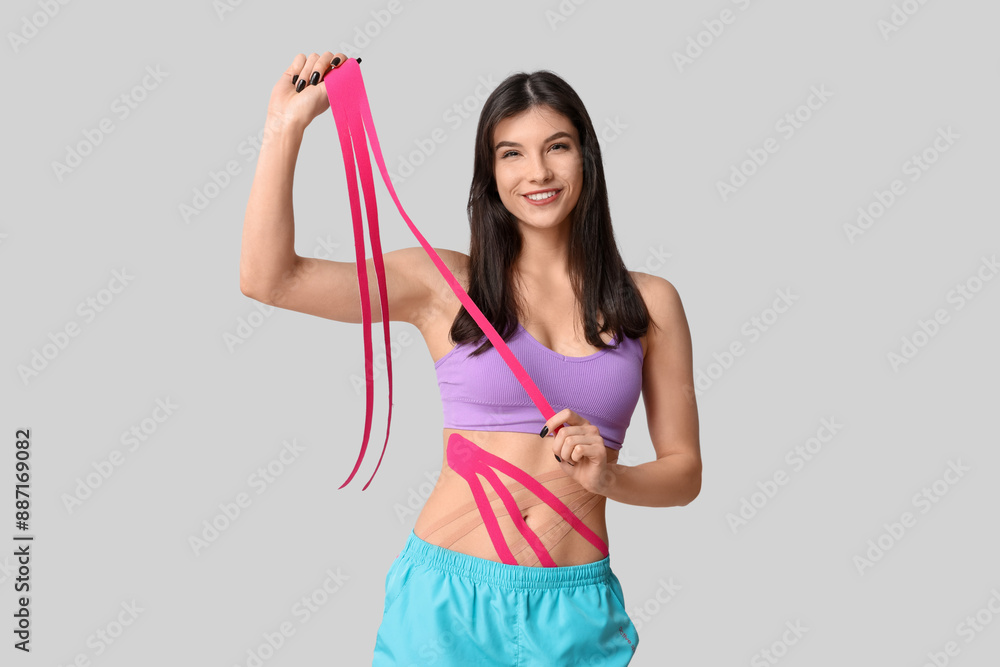 Sporty young woman with physio tape on grey background Sporty young woman with physio tape on grey background