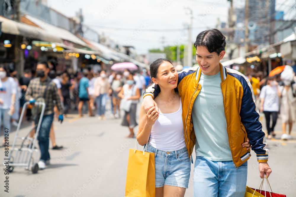 Obraz premium Happy Asian man and woman couple enjoy and fun outdoor lifestyle travel in the city walking and shopping together at Chatuchak weekend street market in Bangkok, Thailand on summer holiday vacation.