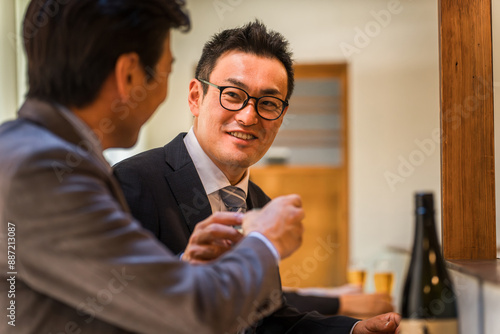 居酒屋・飲み屋のカウンターで部下と楽しくお酒を飲むビジネスマンの男性
 photo