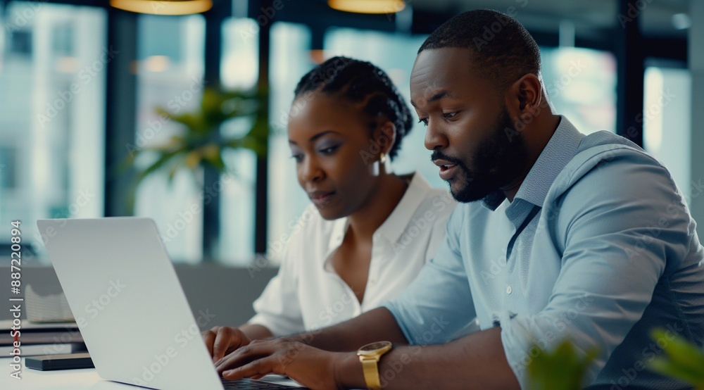 Two african american business people, a man and a woman, working together using a laptop computer while sitting at a desk in an office. The business concept photo for tech and copy space. Two african american business people, a man and a woman, working together using a laptop computer while sitting at a desk in an office. The business concept photo for tech and copy space.