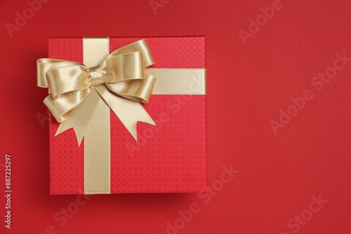 Gift box with bow on red background, top view. Space for text