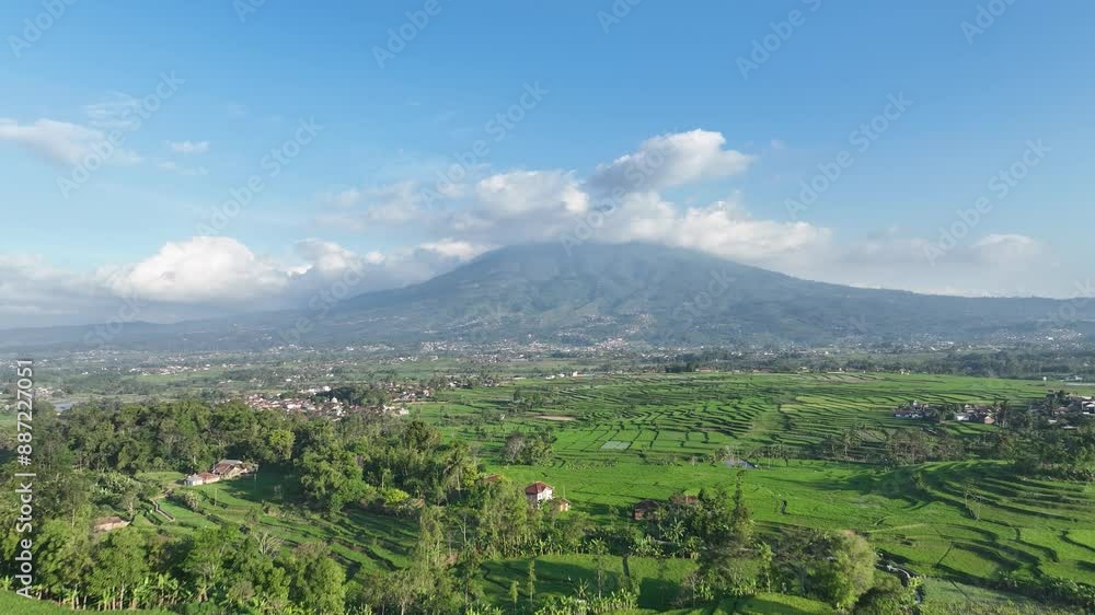 A lush green valley with a large mountain in the background, surrounded by a clear blue sky with scattered clouds, location Garut, Indonesia A lush green valley with a large mountain in the background, surrounded by a clear blue sky with scattered clouds, location Garut, Indonesia