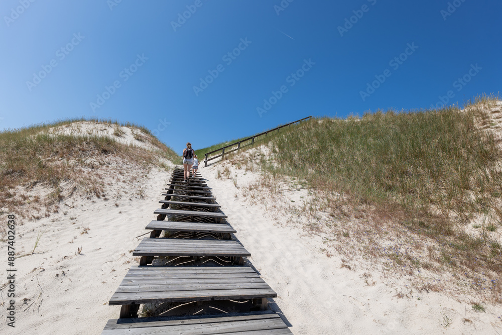 Entrance to the Lubiatowskie Dunes. Mother and daughter climb the stairs to the viewpoint. Beautiful sunny summer weather. Dunes partially covered with grass. Copy space. Lubiatowo, Poland
