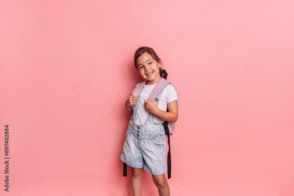 Schoolgirl with a backpack stands in front of a pink background. Schoolgirl with a backpack stands in front of a pink background.