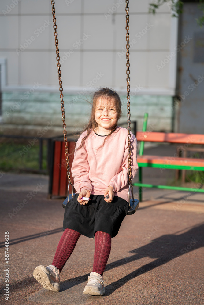 A seven-year-old girl sits on a swing in the yard. A seven-year-old girl sits on a swing in the yard.