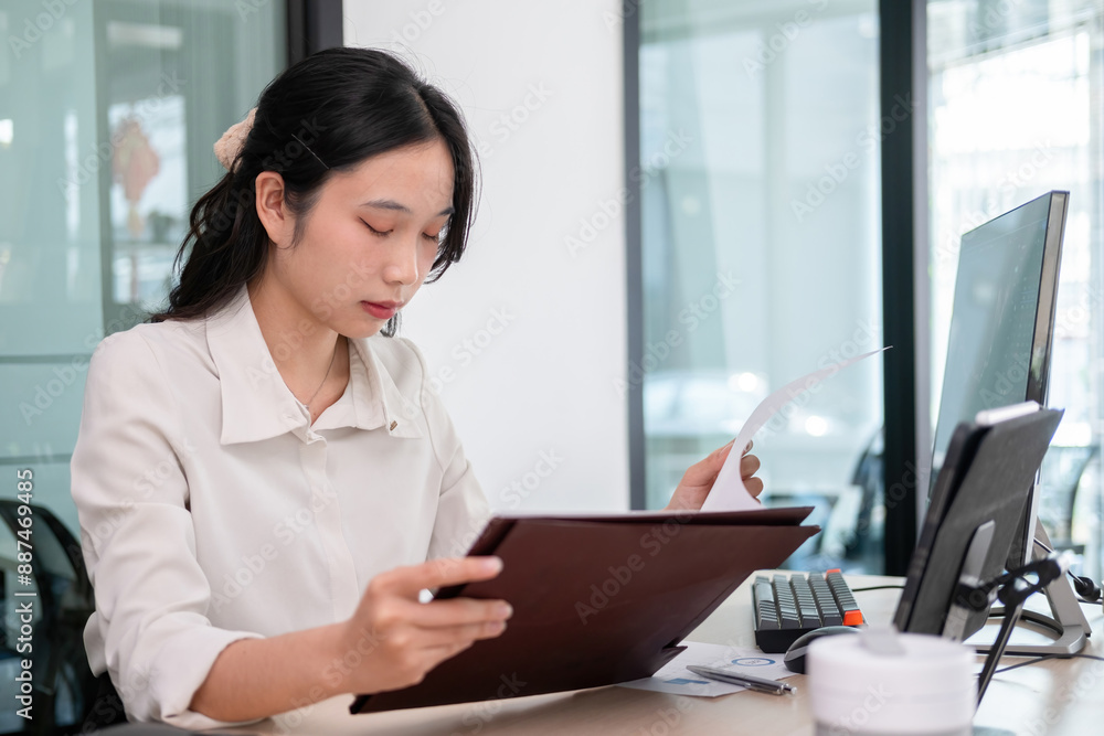 Young woman examines stock graphs and files at office desk
