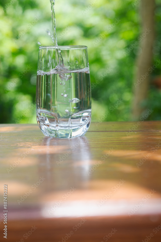 pouring drinking water in to clear glass on wooden table in garden background. pouring drinking water in to clear glass on wooden table in garden background.