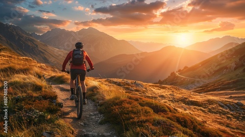 A mountain biker rides along a dirt path, enjoying the sunset over towering peaks