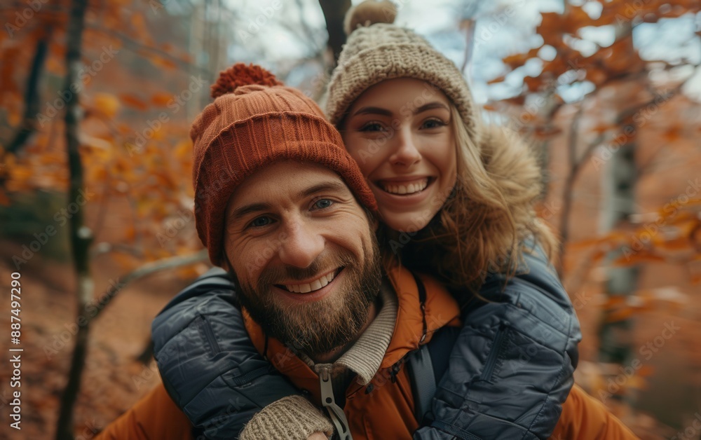A couple smiles for the camera as the man gives his partner a piggyback ride through an autumn forest