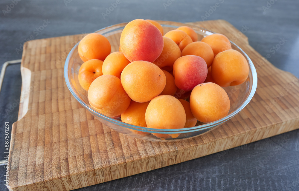 Ripe apricots in a glass bowl on a wooden board