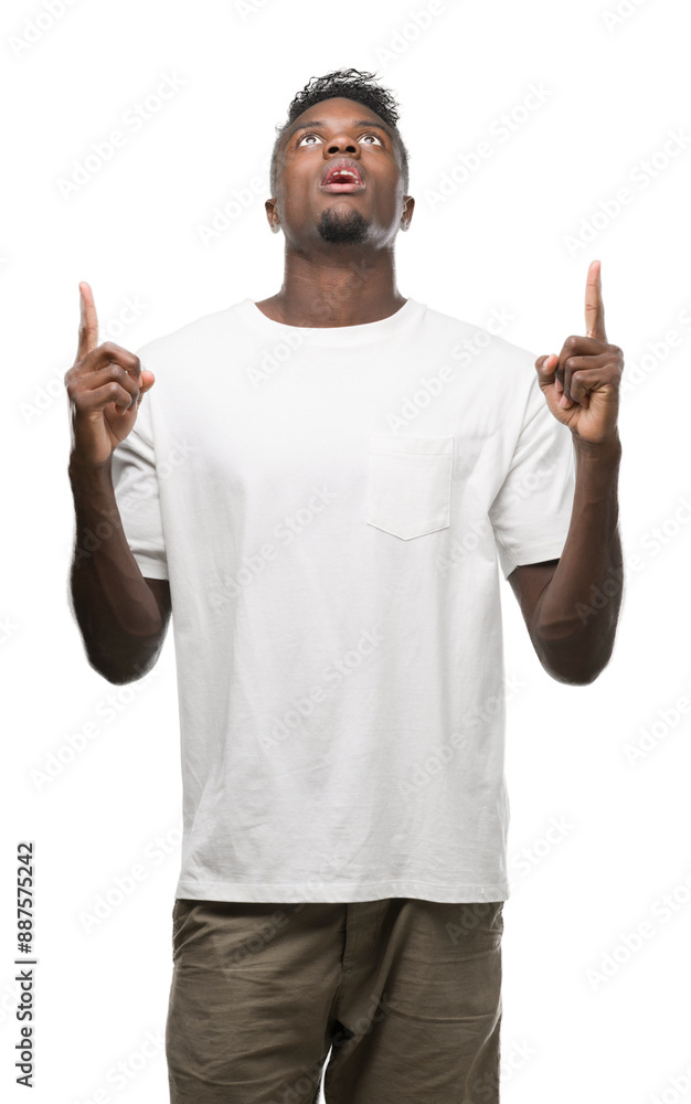 Fototapeta premium Young african american man wearing white t-shirt amazed and surprised looking up and pointing with fingers and raised arms.