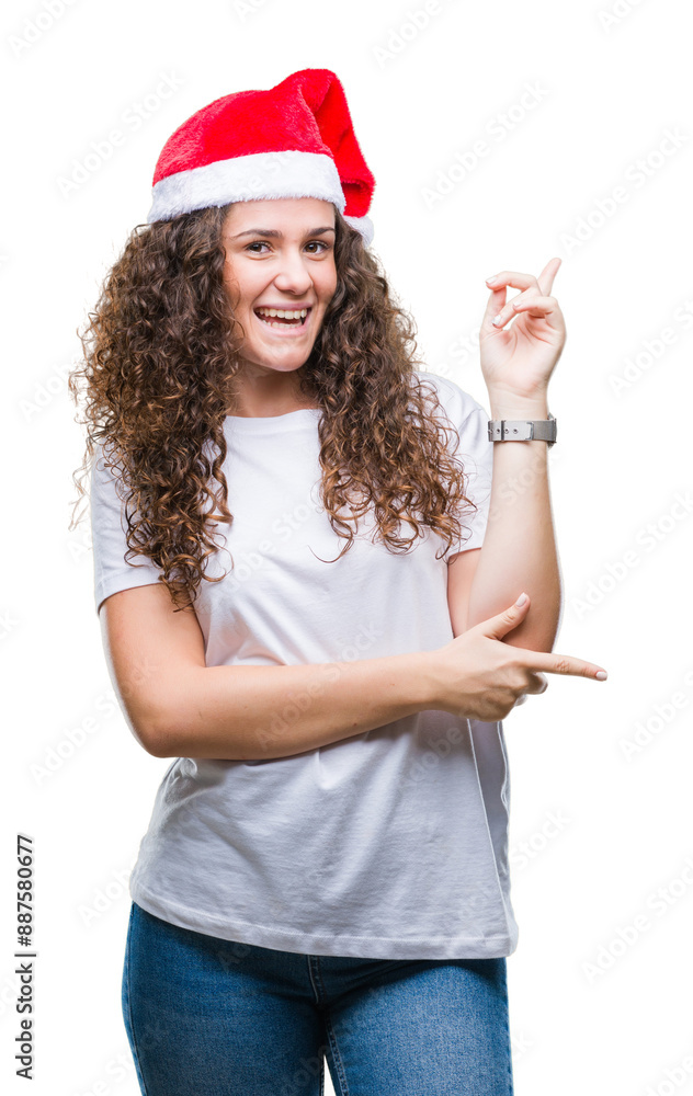 Young brunette girl wearing christmas hat over isolated background with a big smile on face, pointing with hand and finger to the side looking at the camera. Young brunette girl wearing christmas hat over isolated background with a big smile on face, pointing with hand and finger to the side looking at the camera.