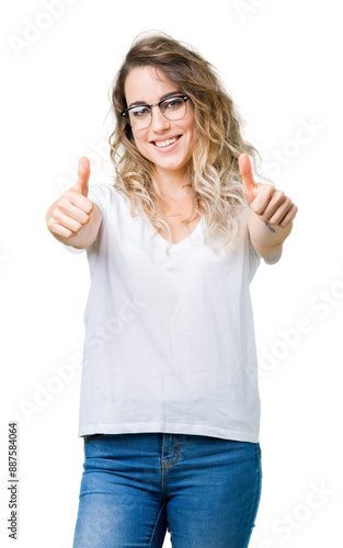 Beautiful young blonde woman wearing glasses over isolated background approving doing positive gesture with hand, thumbs up smiling and happy for success. Looking at the camera, winner gesture.