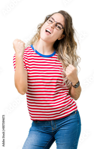 Beautiful young blonde woman wearing glasses over isolated background very happy and excited doing winner gesture with arms raised, smiling and screaming for success. Celebration concept.