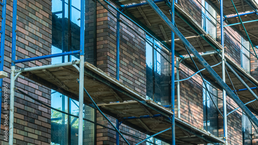Metal scaffolding for cladding the exterior walls of the building. Decorative brick for cladding the exterior walls of the building. Installation work outside the building at a height. Metal scaffolding for cladding the exterior walls of the building. Decorative brick for cladding the exterior walls of the building. Installation work outside the building at a height.