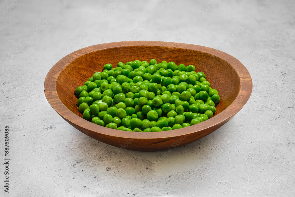 Thawed fresh green peas in a wooden bowl on a stone table Thawed fresh green peas in a wooden bowl on a stone table