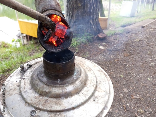 Fotografija Lighting a camping samovar for making hot drinks like tea, coffee in nature near the lake by adding burning coals