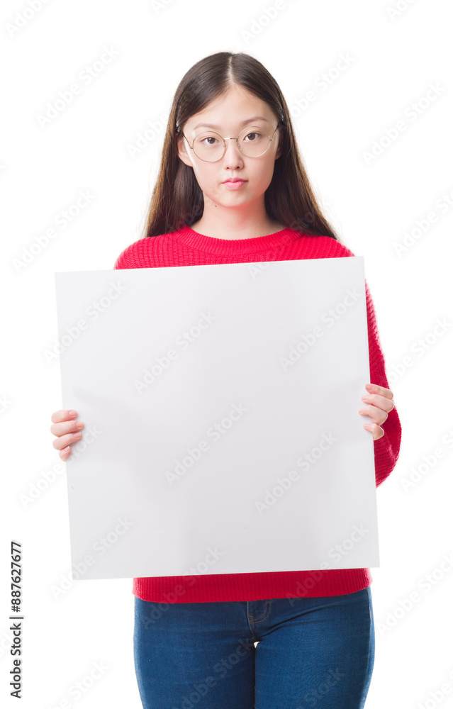 Young Chinese woman over isolated background holding blank banner with a confident expression on smart face thinking serious Young Chinese woman over isolated background holding blank banner with a confident expression on smart face thinking serious