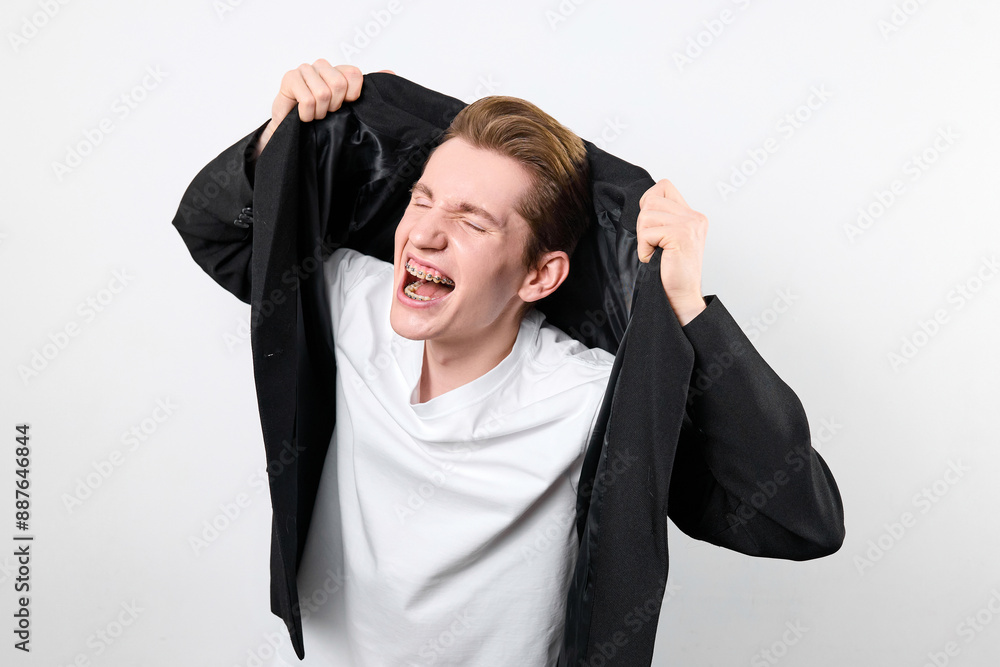 A young man with a joyful expression is captured as he lifts a black blazer above his head with both hands. His open-mouthed smile suggests a moment of elation or victory A young man with a joyful expression is captured as he lifts a black blazer above his head with both hands. His open-mouthed smile suggests a moment of elation or victory