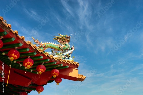 A colorful Chinese Temple pagoda top decorated with lanterns, ornaments and a dragon on the blue sky background.