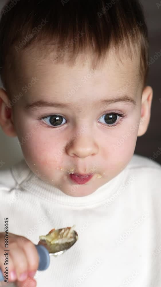Lovely Caucasian baby boy eats himself from a special spoon for kids. Close up. High angle view. Blurred backdrop. Vertical video Lovely Caucasian baby boy eats himself from a special spoon for kids. Close up. High angle view. Blurred backdrop. Vertical video