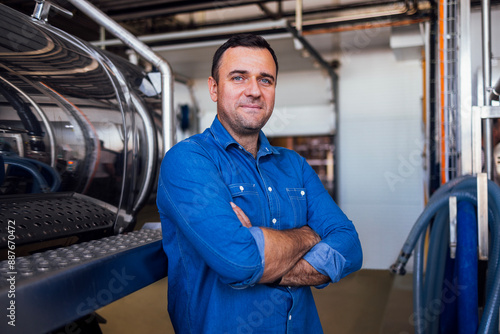 Wallpaper Mural A young smiling man in a denim shirt at the cheese factory. An attractive worker near a milk and a butter making machine. An engineer for the maintenance of a cheese production line. Torontodigital.ca