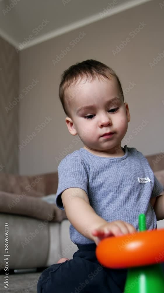 Little Caucasian toddler builds the pyramid. Kid stacks the rings wrong. Low angle view. Vertical video Little Caucasian toddler builds the pyramid. Kid stacks the rings wrong. Low angle view. Vertical video