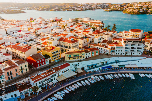 Aerial view of Es Castell traditional town on the Menorca coast with harbor and boats at sunset during summer tourist season. Picturesque balearic town close to Mahon seen from drone