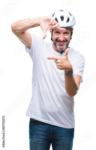 Middle age senior hoary cyclist man wearing bike safety helment isolated background smiling making frame with hands and fingers with happy face. Creativity and photography concept. photo