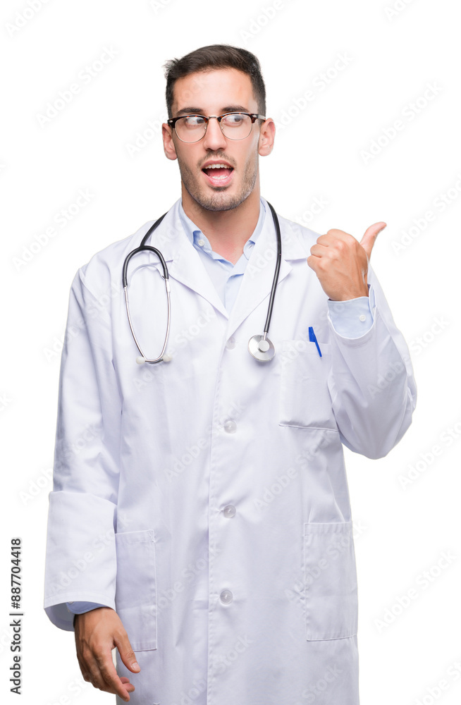 Handsome young doctor man smiling with happy face looking and pointing to the side with thumb up. Handsome young doctor man smiling with happy face looking and pointing to the side with thumb up.