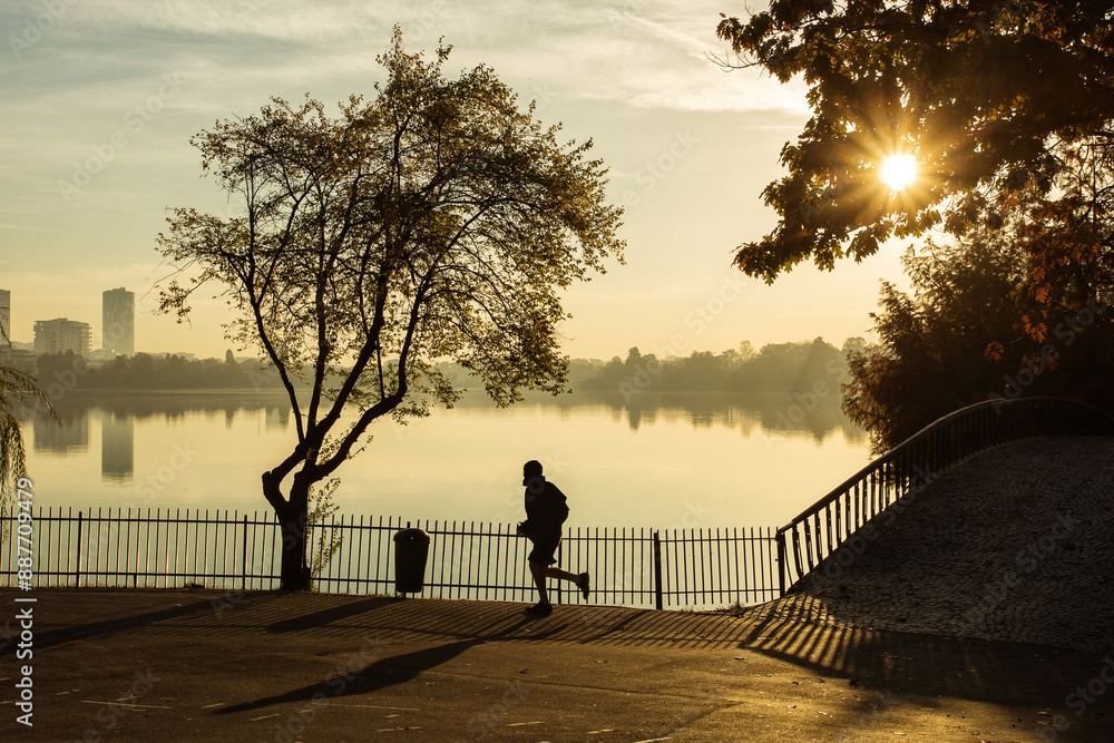 Man running in a park at sunrise with beautiful autumn colors and lake in background