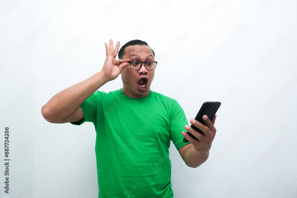 photo of the shocked expression of an Asian man looking at a mobile phone in his hand photo of the shocked expression of an Asian man looking at a mobile phone in his hand