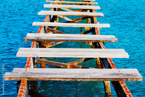 Old wooden footbridge over calm water. The water is calm and the pier is old photo