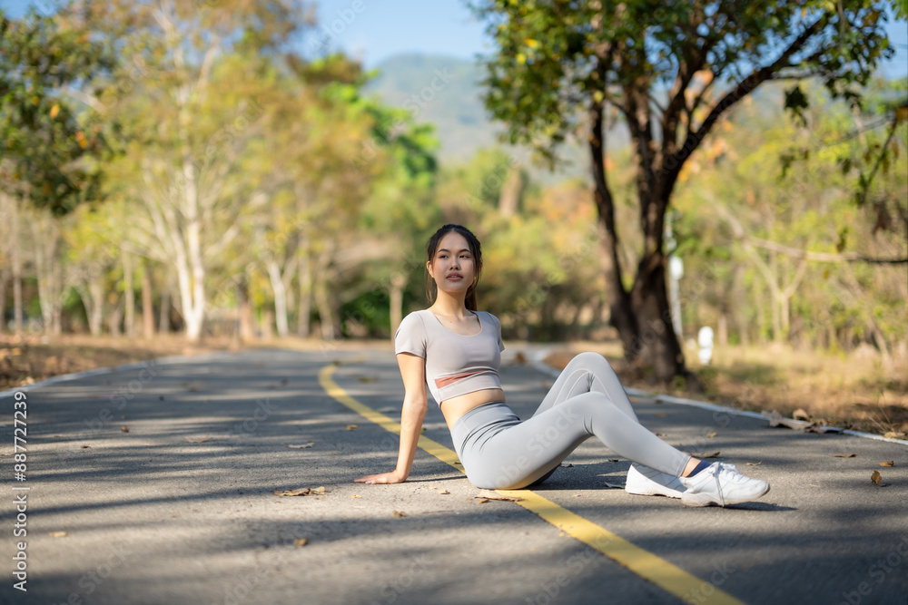 A woman is sitting on the side of a road, wearing a grey shirt and grey pants