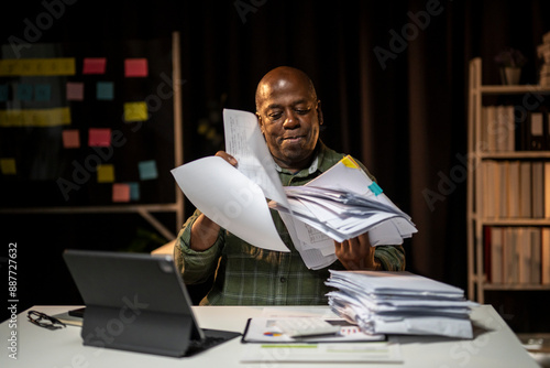 A man is sitting at a desk with a pile of papers in front of him photo