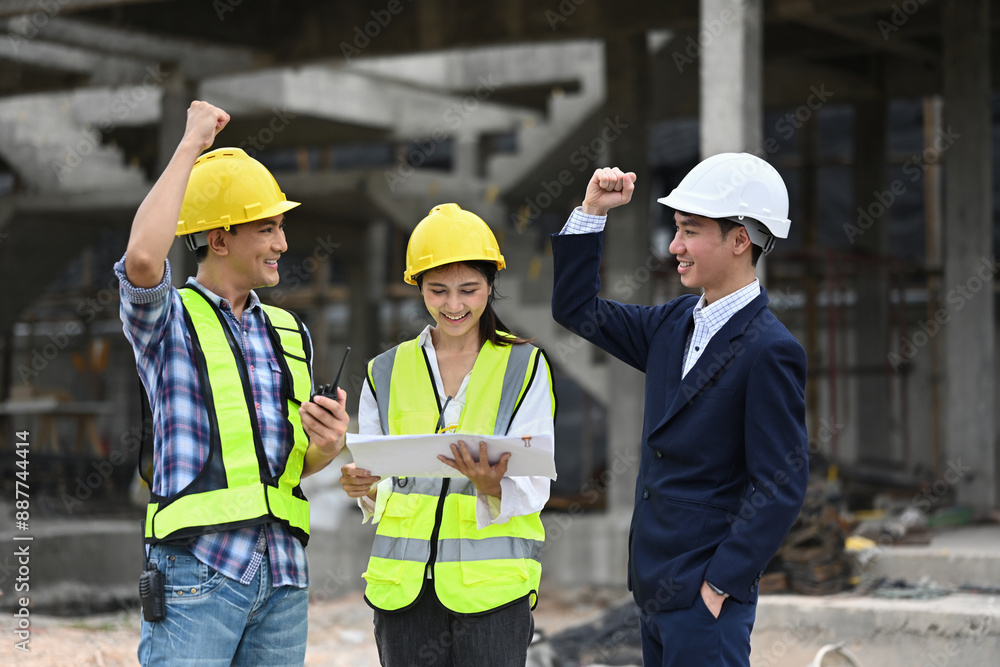 Construction professionals celebrating a success and raising their fists in triumph, at building site Construction professionals celebrating a success and raising their fists in triumph, at building site