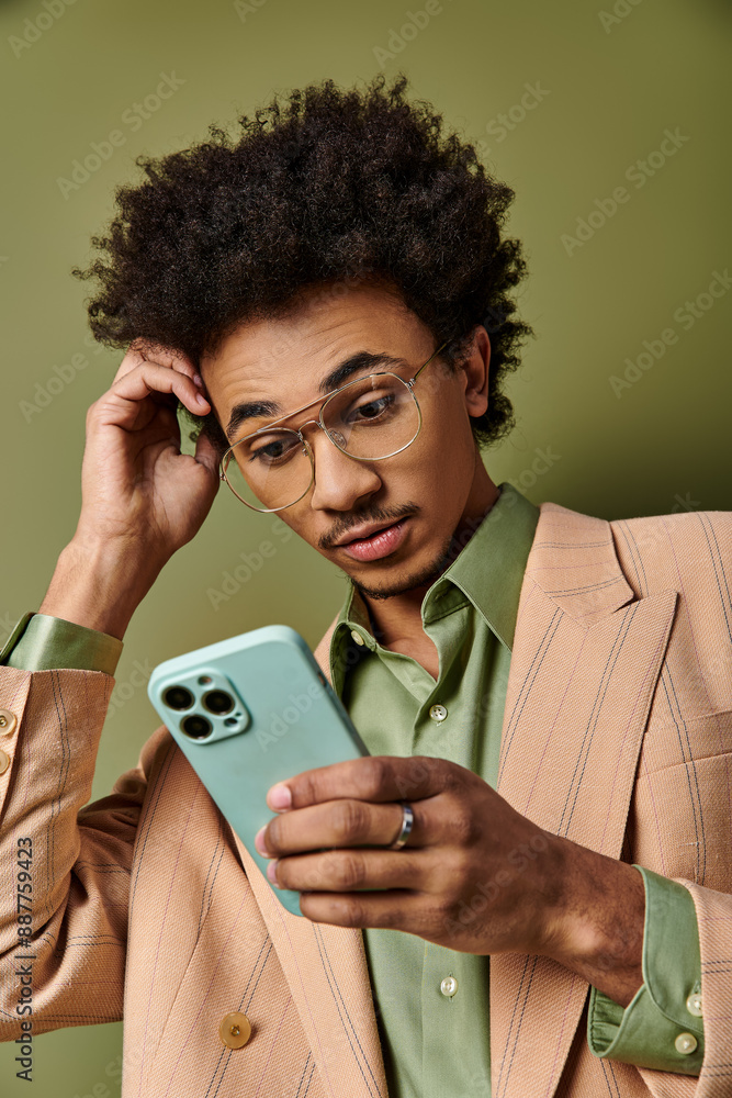 Stylish young African American man in a suit and sunglasses confidently holding a cell phone against a green background. Stylish young African American man in a suit and sunglasses confidently holding a cell phone against a green background.