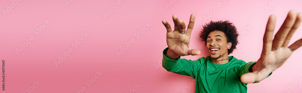 A cheerful young African American man with curly hair in casual wear raising his hands in jubilation on a pink background. A cheerful young African American man with curly hair in casual wear raising his hands in jubilation on a pink background.