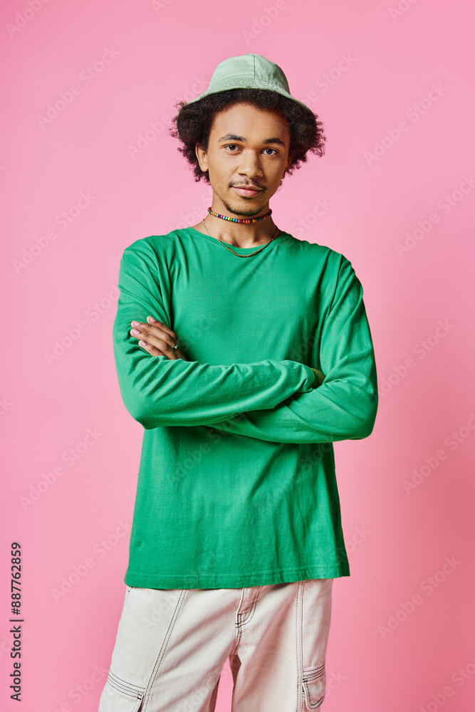 A cheerful young African American man with curly hair wearing a green shirt and pants on a pink background.