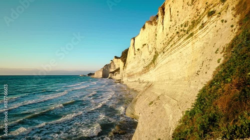 Sandy high cliff and coast of clear blue and turquoise mediterranean sea with waves driven by strong wind at sunset photo