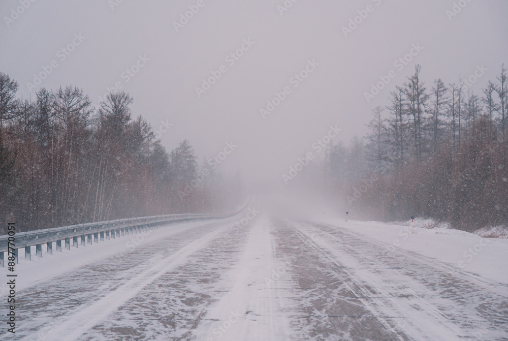 Snow-covered highway through forest during intense winter storm in daytime Snow-covered highway through forest during intense winter storm in daytime