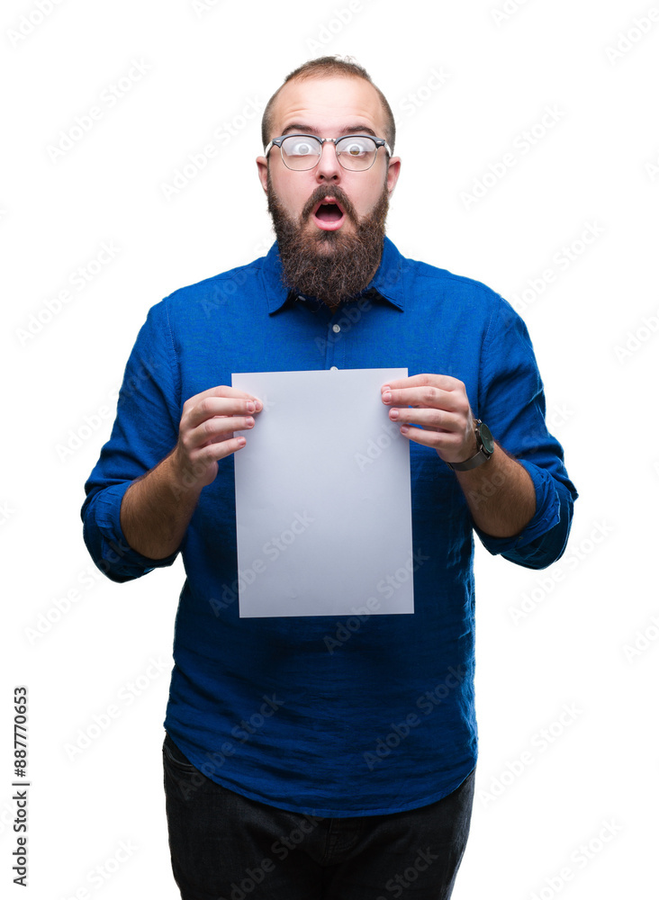 Young hipster man wearing glasses and holding blank paper over isolated background scared in shock with a surprise face, afraid and excited with fear expression Young hipster man wearing glasses and holding blank paper over isolated background scared in shock with a surprise face, afraid and excited with fear expression