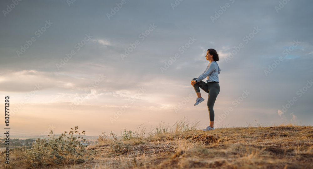 An athletic woman is exercising on a hill at sunset, embracing the tranquil surroundings An athletic woman is exercising on a hill at sunset, embracing the tranquil surroundings