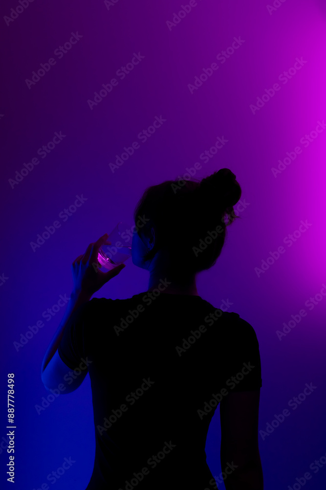 Silhouette of a girl drinking from a glass. Dark profile of mysterious girl drinking from a glass on colored background. Silhouette of a girl drinking from a glass. Dark profile of mysterious girl drinking from a glass on colored background.
