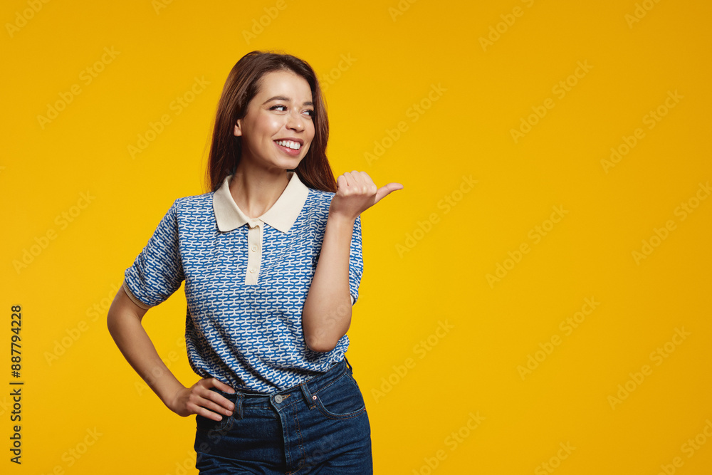 Cheerful smiling woman pointing fingers at copy space and looking away while smiling, standing against yellow background. Advertising concept. Cheerful smiling woman pointing fingers at copy space and looking away while smiling, standing against yellow background. Advertising concept.