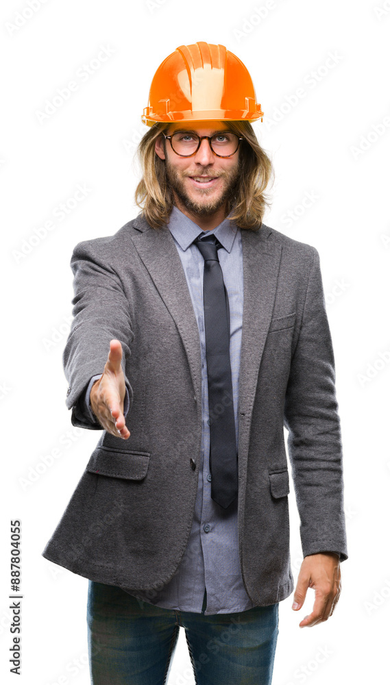 Young handsome architec man with long hair wearing safety helmet over isolated background smiling friendly offering handshake as greeting and welcoming. Successful business. Young handsome architec man with long hair wearing safety helmet over isolated background smiling friendly offering handshake as greeting and welcoming. Successful business.