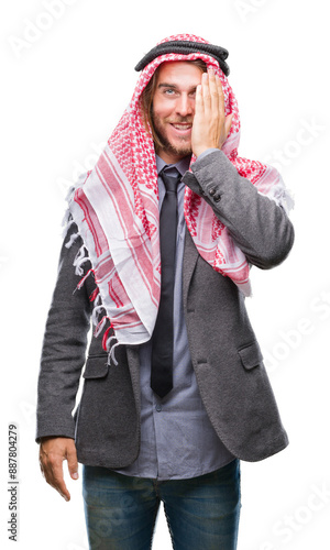 Young handsome arabian man with long hair wearing keffiyeh over isolated background covering one eye with hand with confident smile on face and surprise emotion.