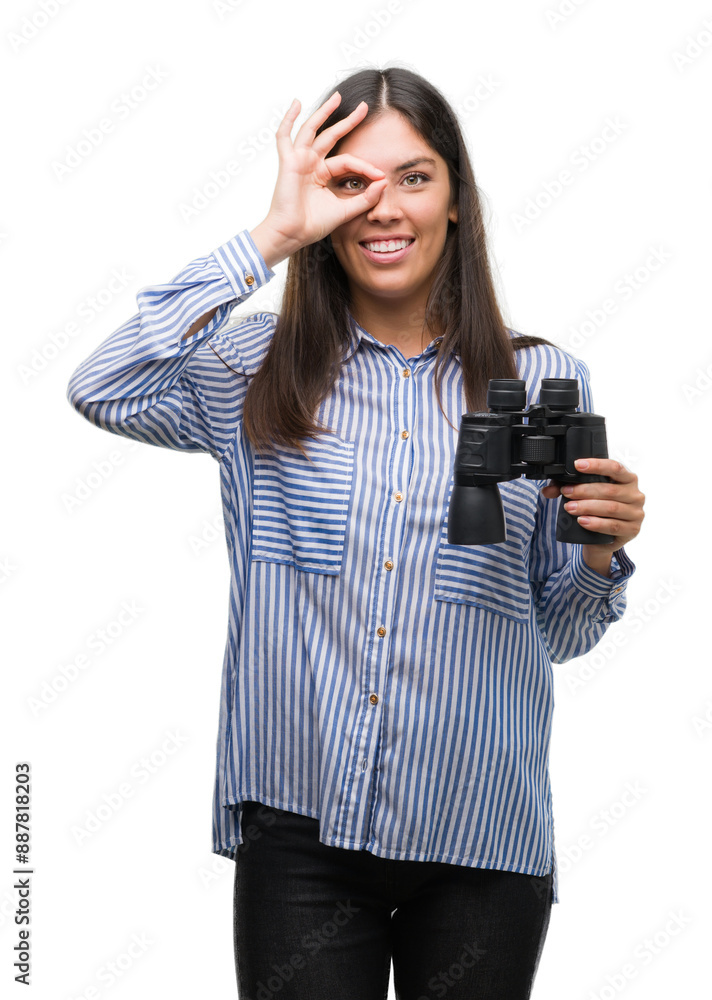 Young hispanic woman holding binoculars with happy face smiling doing ok sign with hand on eye looking through fingers Young hispanic woman holding binoculars with happy face smiling doing ok sign with hand on eye looking through fingers