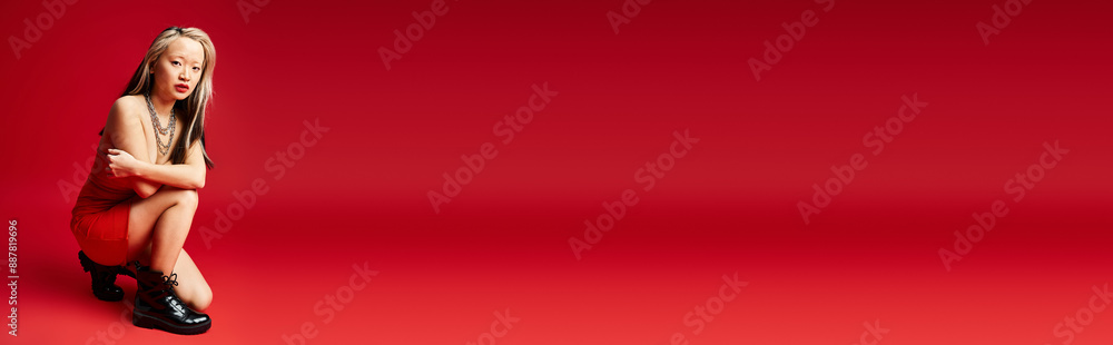 An attractive Asian woman sits gracefully on a red surface with crossed legs. An attractive Asian woman sits gracefully on a red surface with crossed legs.