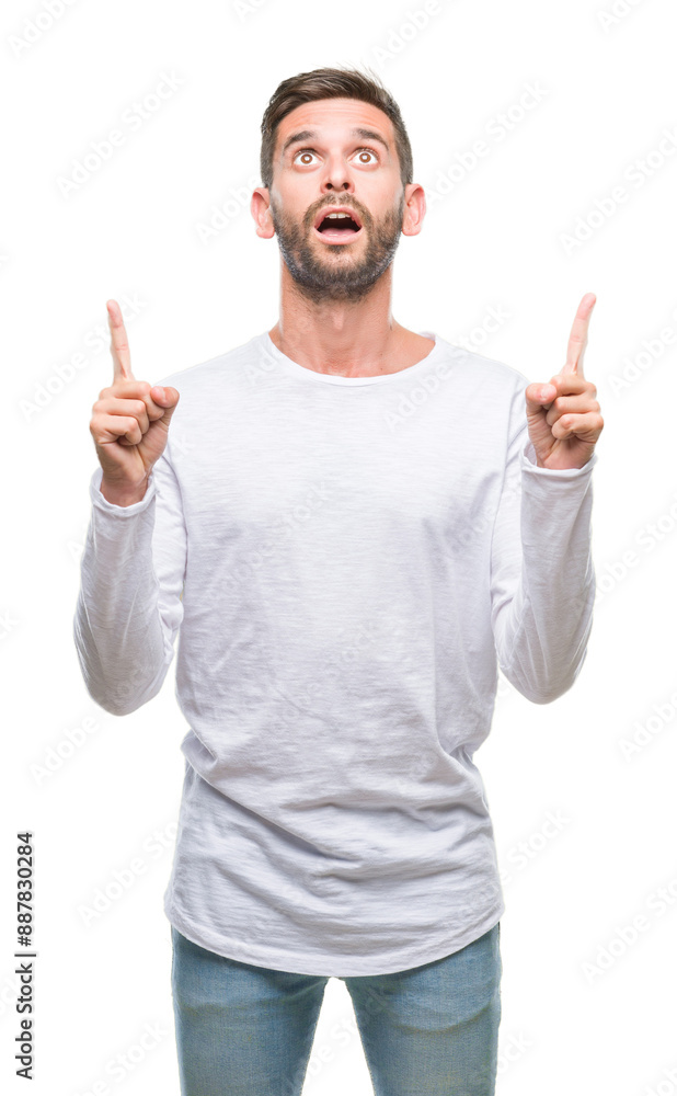 Young handsome man over isolated background amazed and surprised looking up and pointing with fingers and raised arms. Young handsome man over isolated background amazed and surprised looking up and pointing with fingers and raised arms.